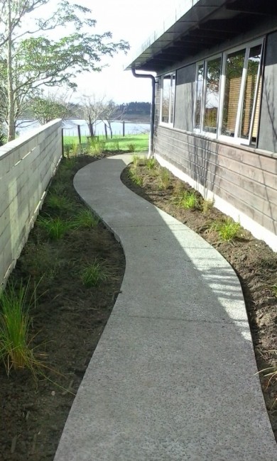 a gently curved exposed aggregate path with native planting and timber fence